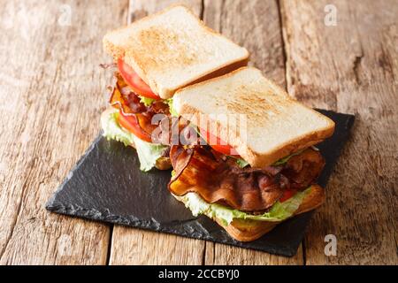 Due panini blt con pancetta, insalata fresca e pomodori sono serviti su una tavola di ardesia sul tavolo. Orizzontale Foto Stock