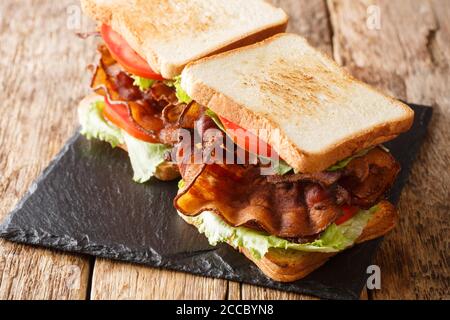 Sandwich americano fast food con pancetta, insalata fresca e pomodori da vicino su una tavola di ardesia sul tavolo. Orizzontale Foto Stock