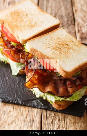 Panino classico con pane tostato blt con pancetta croccante, lattuga ghiacciata fresca e pomodori da primo piano su una tavola di ardesia sul tavolo. Verticale Foto Stock