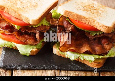 Tradizionale panino americano blt con pancetta, lattuga iceberg e pomodori primo piano su una tavola di ardesia sul tavolo. Orizzontale Foto Stock