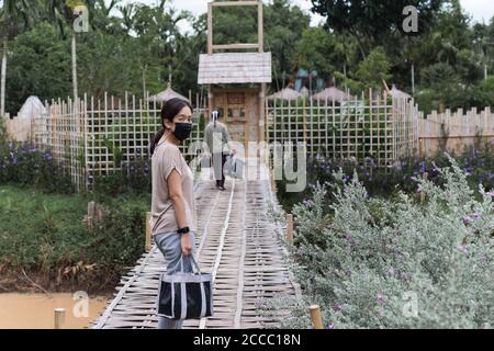 Nuova viaggiatore normale donna con maschera protettiva con facchino portare i bagagli a piedi attraverso il ponte. Foto Stock