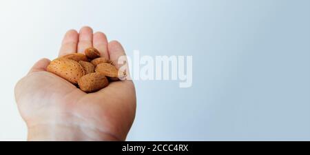 Apri il palmo della mano dell'uomo tenendo una manciata di mandorle in guscio isolato su sfondo chiaro. Copia spazio Foto Stock