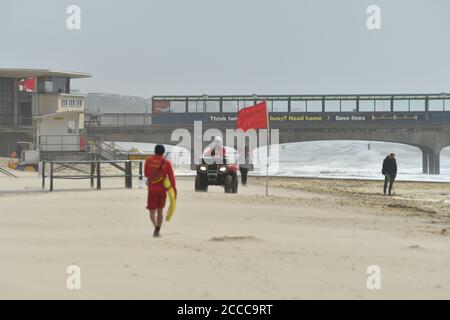 Storm Ellen batte la costa meridionale dell'Inghilterra al culmine della stagione estiva delle vacanze con raffiche di vento fino a 60 mph e un'alta marea. Una bandiera di pericolo rossa che batte nel vento mentre i bagnini pattugliano la spiaggia, Boscombe, Bournemouth, Dorset, UK, 21 agosto 2020 Foto Stock