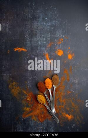 cucchiai con spezie assortite versate su sfondo scuro Foto Stock