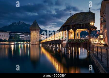 Ponte della Cappella illuminato al crepuscolo. Famoso punto di riferimento contro il Monte Pilatus a Lucerna, Svizzera. Foto Stock