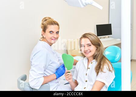 Paziente di sesso femminile seduto sulla poltrona del dentista il dentista  tiene in mano uno specchietto dentale esaminerà i denti del paziente  trattamento dentale professionale