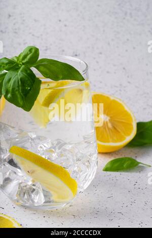 Fuoco selettivo, acqua pura e rinfrescante con limone e basilico in un bicchiere, su sfondo chiaro Foto Stock