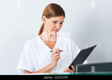 Il medico legge il contratto sulla clipboard con attenzione prima di firmare Foto Stock