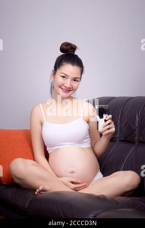 Concetto sano incinta. Un ritratto di una bella donna incinta asiatica beve latte dal bicchiere in mano. Bella Asia modello femminile nei suoi 20 Foto Stock