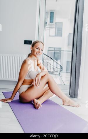 Giovane donna attraente che prende una pausa mentre si esercita a casa. Donna che usa lo smartphone sul tappetino da ginnastica di fronte al suo laptop Foto Stock