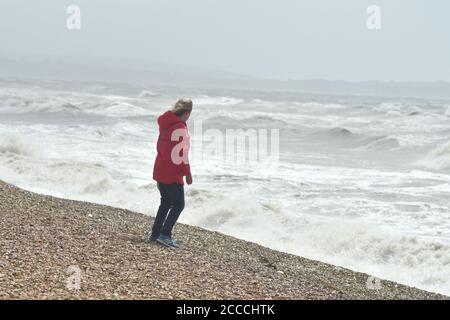 Donna in forte vento a Milford-on-Sea, Hampshire, Regno Unito, agosto, tempo: Tempesta Ellen che batte la costa meridionale dell'Inghilterra al culmine della stagione estiva con raffiche di vento fino a 60 mph e un'alta marea. Foto Stock