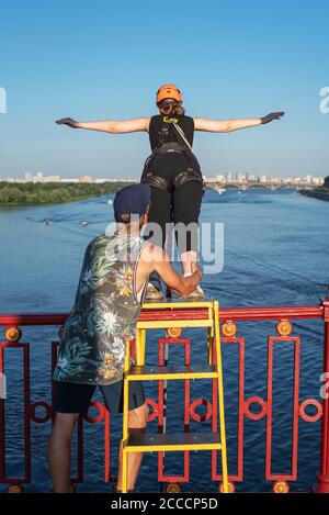 Irriconoscibile ragazza coraggiosa che si prepara a bungee saltare dal ponte sul fiume con il supporto di istruttore. Vista posteriore. Concetto di sport estremi Foto Stock
