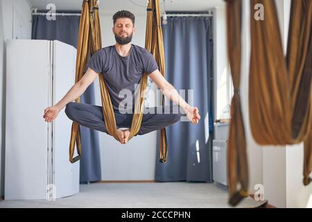 L'uomo medita in un'amaca da yoga aerea Foto Stock
