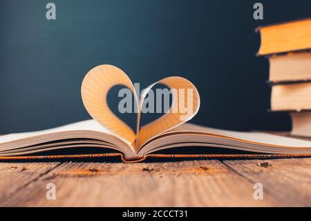 Fogli di un notebook in una gabbia avvolta in Forma di un heart.in lo sfondo è una pila di Libri e un black board.Education concept.Valentine Foto Stock