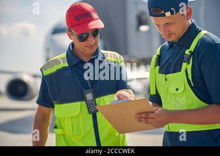 Due lavoratori aeroportuali concentrati che esaminano un documento Foto Stock