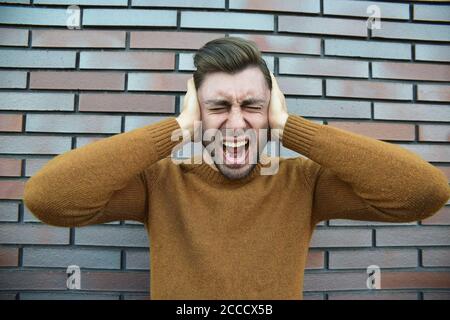 L'uomo sensazione emozioni dolorose, urlando, testimoniando la morte del caro amico, essendo miserabili e devastato, tenendo le palme sulla testa, urla di dolore un Foto Stock