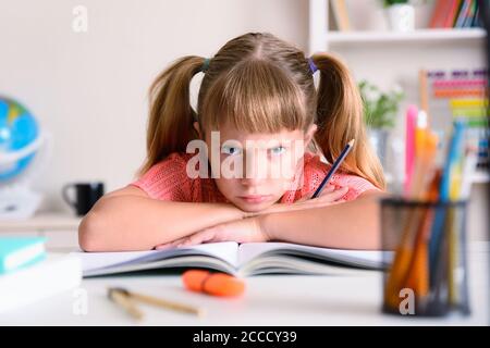 Bambina che studia a casa arrabbiata con braccia incrociate prenota a casa al banco di studio Foto Stock