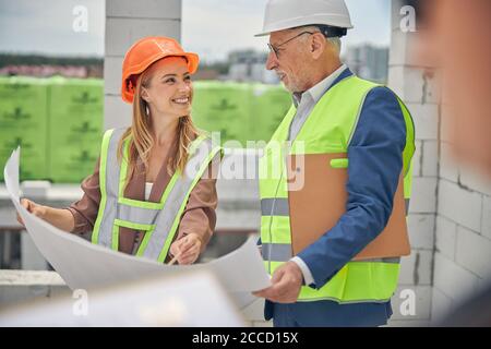 Signora allegra in un casco che comunica con un caposquadra Foto Stock