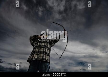 Cacciatore ricreativo in cappello tiro longbow. Tiro naturale di tiro con l'arco. Foto Stock