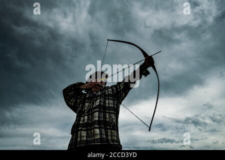 Cacciatore ricreativo in cappello tiro longbow. Tiro naturale di tiro con l'arco. Foto Stock