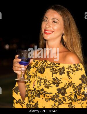 Donna sorridente . Isolated.giovane donna adulta che tiene un bicchiere di vino blu sorridente alla macchina fotografica. Immagine stock. Foto Stock