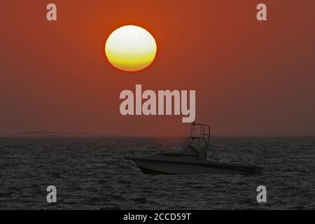 Tramonto sull'oceano Indiano a Ifaty in Madagascar. Una barca a motore che galleggia in mare aperto di fronte al sole che tramonta. Foto Stock