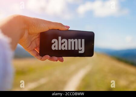 Donna escursionista che prende selfie con smartphone in montagna su cima collina. Primo piano dello schermo del telefono cellulare. Spazio mockup Foto Stock