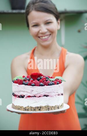 Giovane donna in giardino tiene una cheesecake lampone Foto Stock