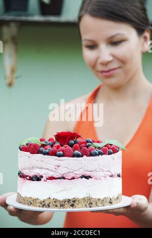 Giovane donna in giardino tiene una cheesecake lampone Foto Stock