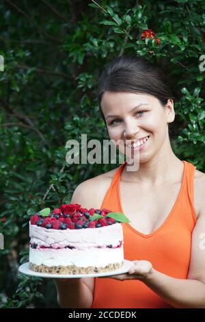 Giovane donna in giardino tiene una cheesecake lampone Foto Stock