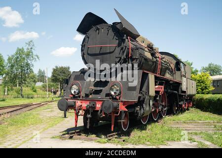 Grande locomotiva a vapore d'epoca, dettaglio ruota in acciaio verniciata di rosso da vicino. Treno a vapore a carbone su un siding. Macchinario ferroviario pesante gigantesco classico Foto Stock