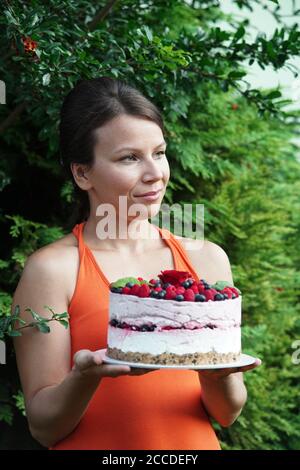 Giovane donna in giardino tiene una cheesecake lampone Foto Stock