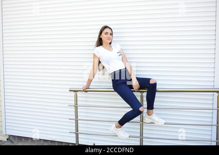 Bella giovane donna che indossa jeans, t-shirt bianca, in piedi sulla strada. Foto vicino recinto di ferro Foto Stock
