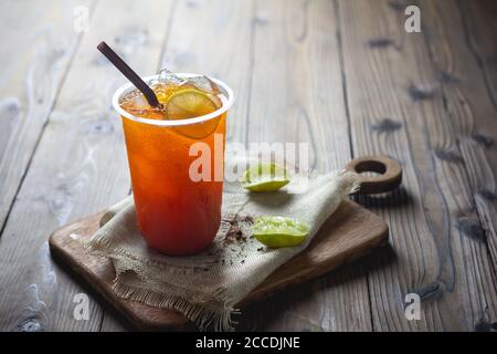 tè ghiacciato con fetta di limone in tazza di plastica lo sfondo in legno Foto Stock