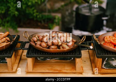 Metà di patate fritte, in una padella sul fornello, con salsicce fritte e anelli di pomodoro tritati su un tavolo a buffet presso l'hotel. Foto Stock