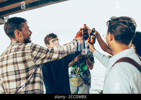 Gruppo di amici che festeggiano, riposano, si divertono e festeggiano in estate. Giovani che bevono birra, parlano, ridono. Guarda felice e allegro. Tempo di festa, vacanza, estate, unità e amicizia. Foto Stock