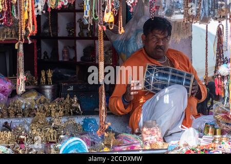 Orchha, Madhya Pradesh, India - Marzo 2019: Un negoziante maschile seduto nel suo negozio di artigianato e suonando un tabla, uno strumento musicale indiano a tamburo. Foto Stock