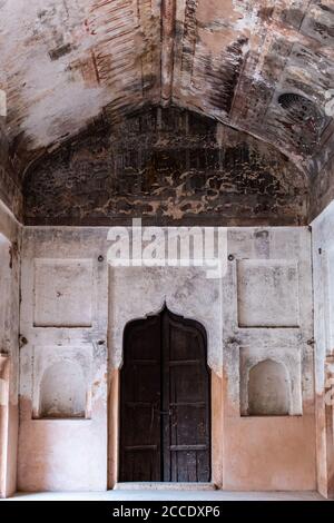 Orchha, Madhya Pradesh, India - Marzo 2019: Le pareti sbiadite con nicchie arcuate e una porta di legno di una sala all'interno dell'antico Raja Mahal nell'Orchha Foto Stock