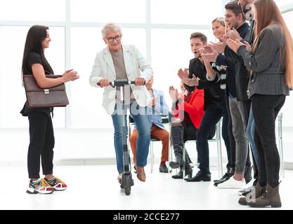 uomo d'affari maturo in tuta che guida uno scooter elettrico dentro ufficio Foto Stock