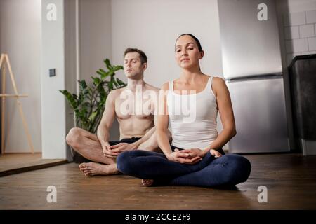 sposato coppia caucasica meditando, fare esercizi di yoga a casa insieme, sedersi con le gambe incrociate in una posa sul pavimento. coppia conduce uno stile di vita sano, Foto Stock