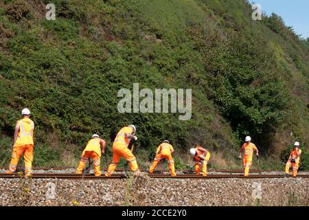 Un gruppo, o gang, o Netwok Rail lavoratori che svolgono lavori di manutenzione su una linea ferroviaria in diretta. Gli uomini stanno liberando i detriti dalla pista usando i rastrelli Foto Stock