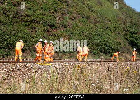Un gruppo, o una banda, o Netwok Rail, lavoratori che svolgono lavori di manutenzione su una pista ferroviaria in tempo reale. Gli operatori stanno eliminando i detriti dal cingolo Foto Stock