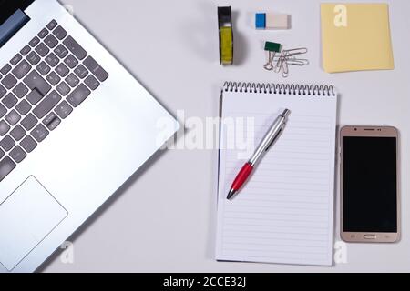 Moderno tavolo da lavoro bianco con computer portatile, smartphone e altri accessori. Vista dall'alto, disposizione piatta. Foto Stock