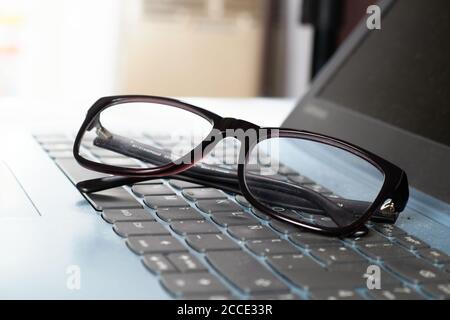 Occhiali sulla tastiera del computer con l'effetto della luce. Primo piano di occhiali neri e un computer portatile. Lavoro in ufficio, business e tecnologia. Foto Stock