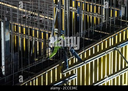 Austin, TX USA 25 luglio 2020: Il lavoratore di costruzione che indossa attrezzatura di sicurezza e la copertura del viso prepara la cassaforma per la colonna di cemento sul garage di alta torre che sale nel quartiere di Rainey Street vicino al centro di Austin. Foto Stock