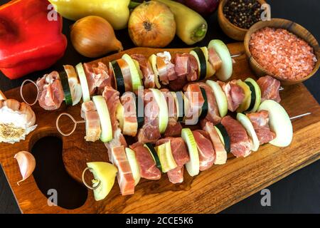 Pezzi di maiale crudi spiediti su bastoncini d'acciaio. Preparazione per barbecue estivo. Kebab di carne colorati preparati al momento con cipolla e pancetta. Carne cruda. Foto Stock