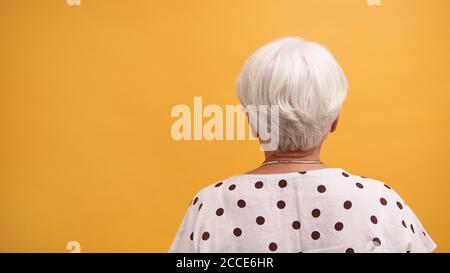 Vista posteriore di una donna senior con capelli grigi isolata sullo sfondo arancione. Foto di alta qualità Foto Stock