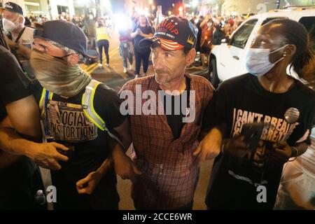 Tulsa, OK, Stati Uniti. 20 giugno 2020 : UN sostenitore di Trump e i manifestanti della materia Black Lives collegano le armi per impedire alla folla di avvicinarsi agli ufficiali di polizia. Foto Stock