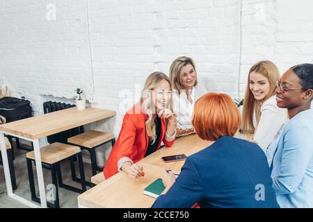 Lavoro di squadra processo. Multirazziale del gruppo di giovani donne che collaborano in open space office. I capelli rossi Mentor coach a parlare ai giovani, insegnamento aud Foto Stock