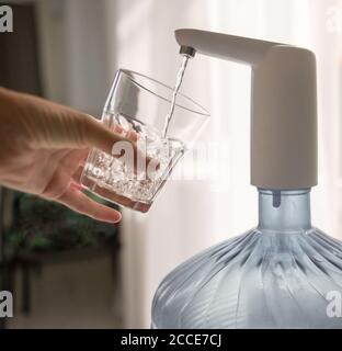 la mano con un bicchiere versa l'acqua dal refrigeratore Foto Stock